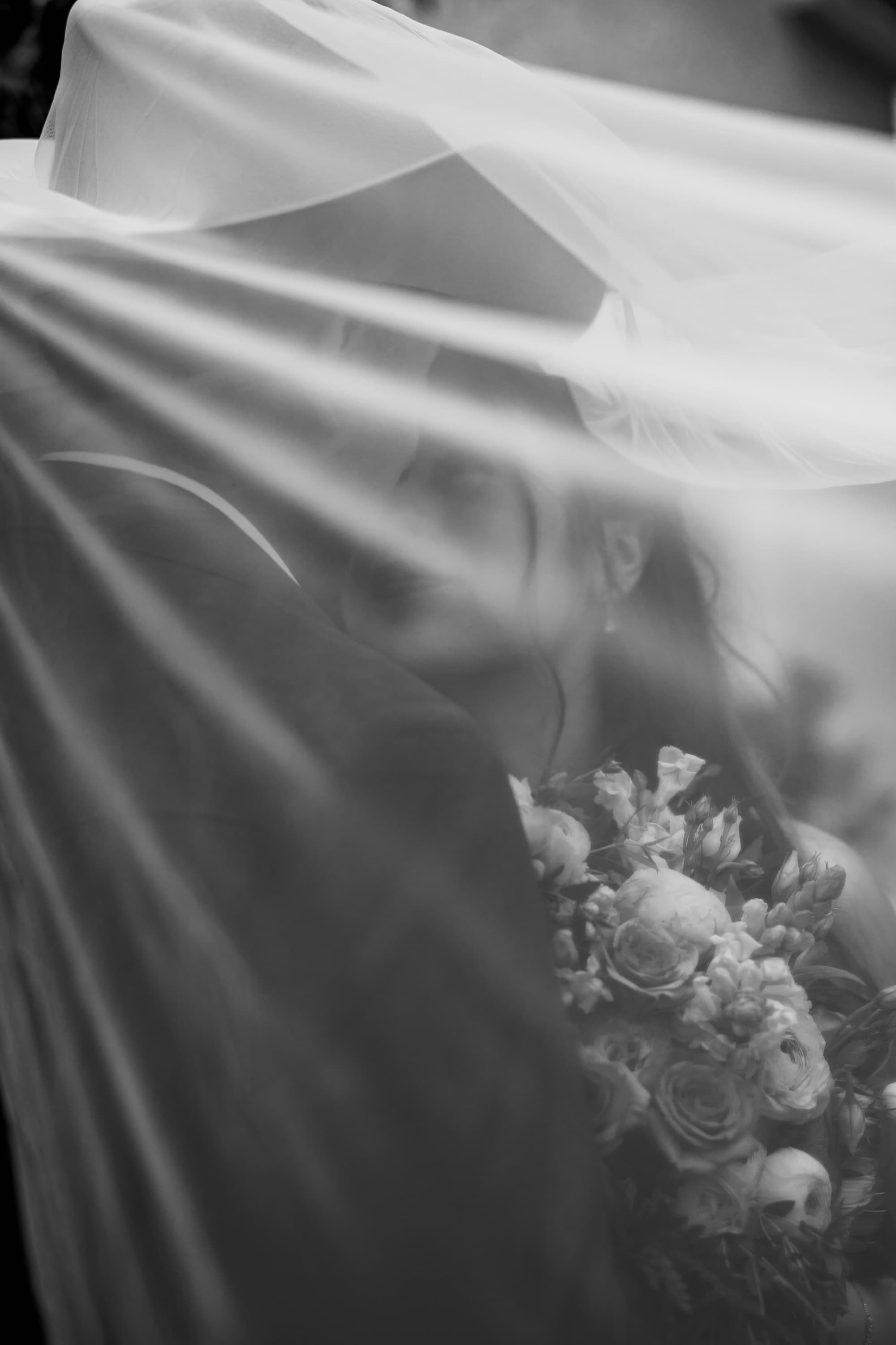A bride and groom beneath her veil, the bouquet catching the light — a wedding photographed in black and white